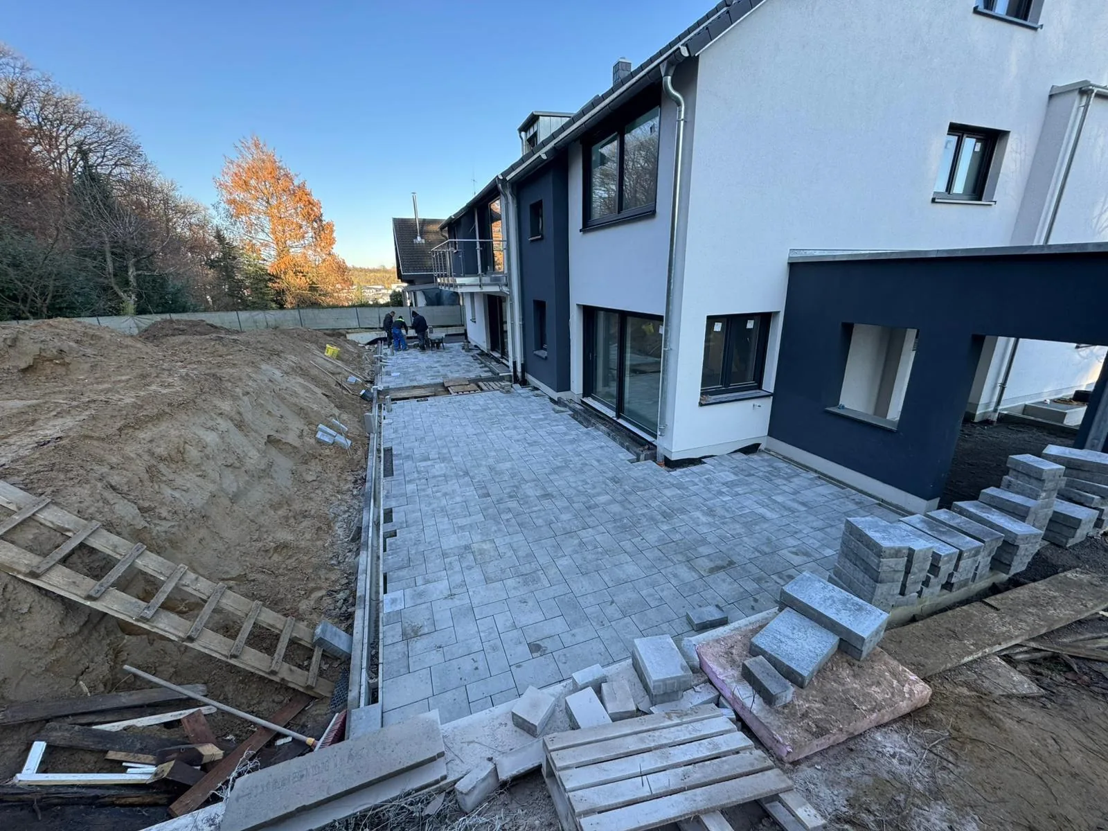 Helle Pflasterfläche entlang eines Wohngebäudes mit angrenzendem Erdreich